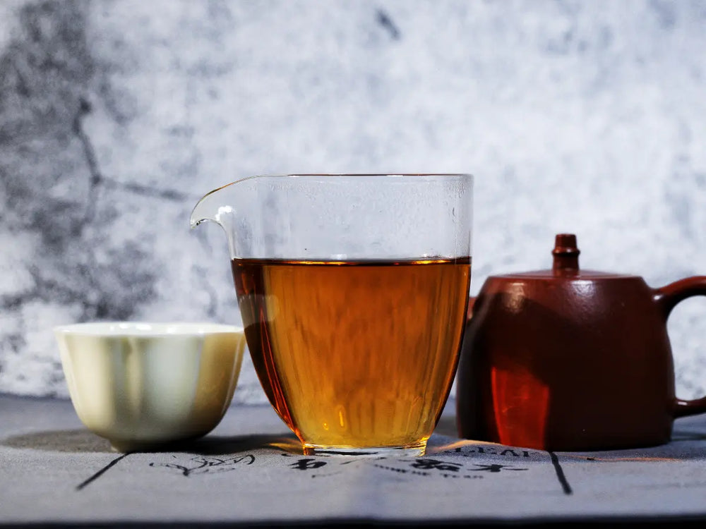 Amber Fu tea in a glass pitcher beside a clay teapot and porcelain tasting cup