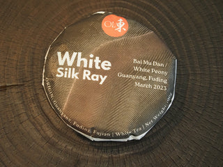 Front view of Silk Ray Fuding Bai Mu Dan white tea cake wrapped in minimalist laboratory-style paper packaging, March 2023 harvest.