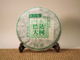 Jing Chang Hao Bada Ancient Trees 2013 raw Pu-erh cake in green-printed Dai mulberry paper wrapper, on a wooden tea stand