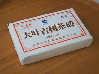 Front view of the wrapped 2013 Dry-Aged Lincang Ripe Pu-erh Ancient Tree Tea Brick showing its traditional paper packaging and Chinese characters.