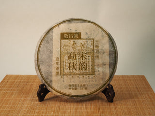 Jing Chang Hao Mengsong Autumn Harvest 2013 raw Pu-erh 357g cake in traditional printed paper wrapper, displayed on a wooden tea stand