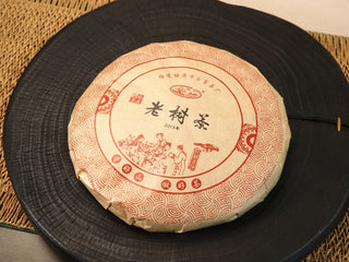 2013 Fuding Sun-Dried Shou Mei 300g cake — front paper wrap with red Chinese pattern, displayed on a dark wooden tray.