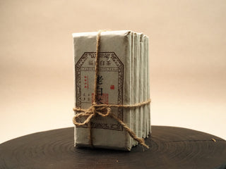 Single 2014 sun-dried Fuding Shou Mei 100g waffle cake in kraft paper wrapper tied with string, Fuding white tea label visible, side view.