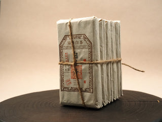 Bundle of ten 2014 sun-dried Fuding White Peony 100g waffle cakes wrapped in kraft paper and tied with hemp rope on a wooden tray.