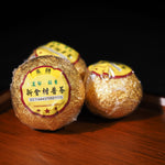 Wrapped whole Da Hong Gan citrus Pu-erh tea with traditional yellow label on wooden tray.