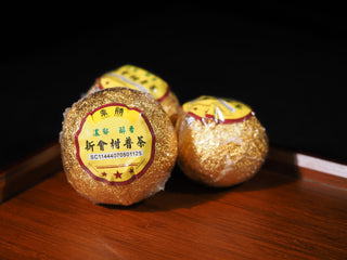 Wrapped whole Da Hong Gan citrus Pu-erh tea with traditional yellow label on wooden tray.