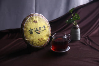 Full view of 2017 Lincang Gongting Ripe Puerh Tea 400g cake with a glass of dark red tea liquor.