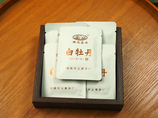 Four sealed sachets of 2018 indoor-withered Fuding White Peony compressed tea biscuits stacked in a wooden box with gold label.