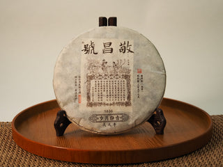 Jing Chang Hao Quiet Years 2018 raw Pu-erh 357g cake in traditional printed paper wrapper with red seal marks, displayed on a wooden tea stand
