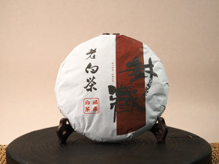 2018 sun-dried Fuding Shou Mei 350g cake in cream paper wrapper with red Shou character, aged white tea label and Fuding seal, on wooden stand.