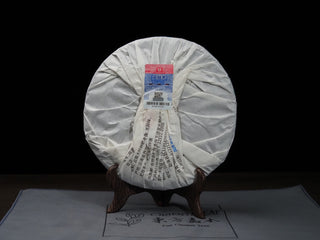 Back view of wrapped 2021 Dayi Guanchao Raw Puerh Tea Cake Batch 2101 with white protective paper packaging and specification label.
