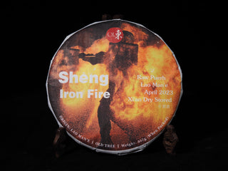 Front view of the 2023 Iron Fire Lao Man'e raw Puerh tea cake wrapped in its fiery Tiehua molten iron art wrapper on a wooden stand.