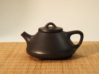 Fengming Ziye Shipiao Yixing teapot in raw Shihuang clay, front side view with spout and arched bridge knob on a bamboo mat