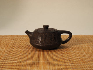 Guyun Shipiao Yixing teapot in coarse antique bronze clay, front view with carved calligraphy on a bamboo mat