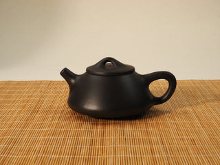 Black Zhu Ni Ziye Shipiao Yixing teapot, side view with spout and bridge knob lid, resting on a bamboo mat