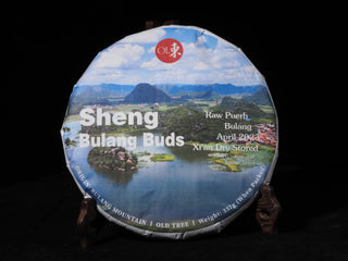 Front view of Sheng Bulang Buds 2023 raw Puerh tea cake wrapped in artisanal paper wrapper on a wooden stand.