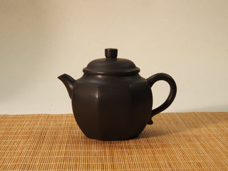 Shihuang Bafang Yixing teapot in dark black clay, front side view with spout facing left, sitting on bamboo mat