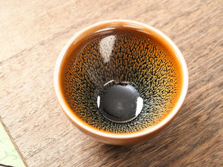 Top view of a Shu Kou yellow partridge Jianzhan tea bowl on a wooden table, showing fine rust-orange speckles across the dark interior with a brighter rim band.
