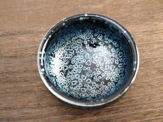 Top view of a Xiang Lu Jianzhan tea bowl with silver oil-spot crystals on a black glaze, resting on a wooden surface.