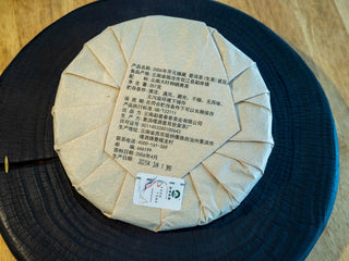 Back view of the 2006 vintage raw Puerh tea cake showing traditional paper wrapping foldings and product label.