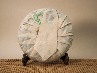 Back of the wrapped Jing Chang Hao Bada Ancient Trees 2013 raw Pu-erh cake with green product label, folded Dai paper wrapper