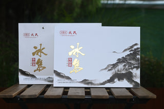Two white gift boxes of Mengku Rongshi 2020 Bingdao Aged Raw Pu-erh coin cakes on a wooden table.