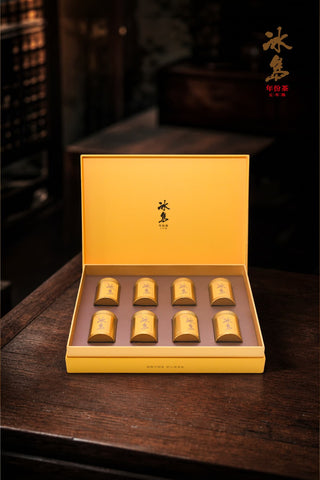 Open presentation box revealing 8 golden tins of Mengku Rongshi Bingdao Aged Ripe Pu-erh coin cakes in 2x4 arrangement.