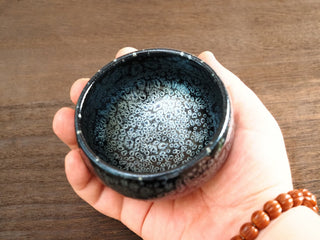 Top view held in hand of a Da Chan Ding Jianzhan tea bowl, showing the interior densely covered with silver oil-spot crystals.