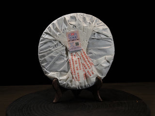 Traditional folded paper backing of the 2017 Dayi 7452 ripe puerh tea cake with a quality certification label on a wooden stand.