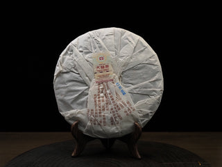 Back packaging of the 2019 Dayi 7592 ripe puerh tea cake wrapped in traditional pleated cotton paper on a display stand.