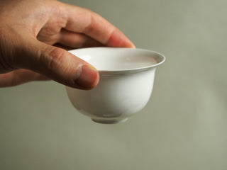 Hand holding pure white egg-shell porcelain gaiwan bowl, showing thin walls and smooth glazed flared rim