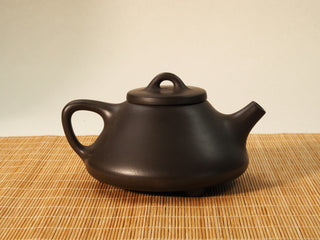Fengming Ziye Shipiao Yixing teapot reverse side view showing handle and short spout, dark brown clay body on a bamboo mat