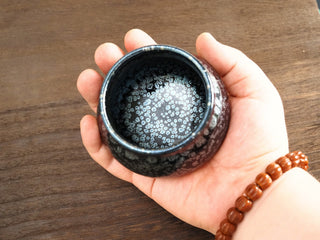 Fo Du Sky Eye Jianzhan tea bowl held in hand showing the interior densely covered with silver oil-spot crystals like a starry sky.
