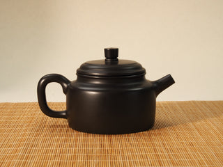 Heini Dezhong Yixing teapot reverse side view showing the ear-shaped handle and cylindrical black clay body on bamboo mat