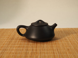 Black Zhu Ni Ziye Shipiao Yixing teapot viewed from the opposite side with handle and short spout on a bamboo mat