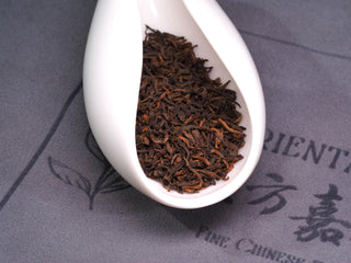 A close-up of premium Imperial Puerh golden buds in a white tea scoop, highlighting the high-grade loose leaf quality.
