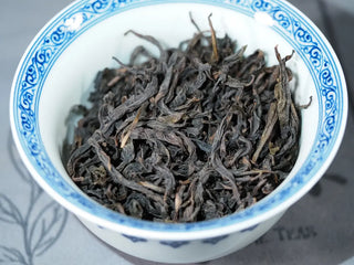 Close-up of Jin Guanyin (204) Floral Wuyi Rock Oolong dry tea in a gaiwan, highlighting the glossy, tightly rolled leaves and orchid–osmanthus fragrance character.