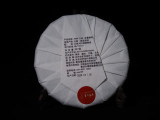 Back view of the Lao Man'e ancient tree raw Puerh cake showing the traditional Chinese paper wrapping folds and security label.