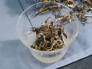 Premium Grade 1 yellow tea buds placed in a clear glass vessel for brewing.