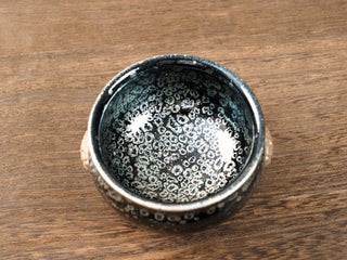 Top view of a Rui Shou sky eye oil spot Jianzhan tea bowl on a wooden table, showing dense ring-shaped silver crystals across a deep black interior.