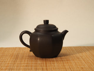 Shihuang Bafang Yixing teapot back view with handle on left, dark eight-faceted body resting on a bamboo mat