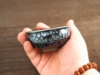 Side view of a Xiang Lu Jianzhan tea bowl held in hand, showing the short incense-burner form and dense silver oil-spot pattern on the exterior.