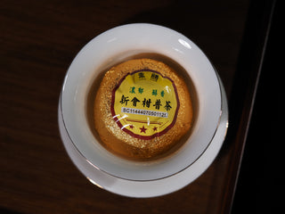 Single wrapped Xinhui citrus Pu-erh tea cake sitting perfectly in a white porcelain Gaiwan bowl.