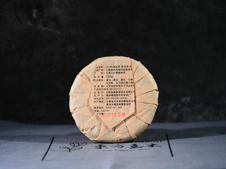 Back view of Yiwu Raw Pu-erh Cake – 2013 Spring Tea, Hand-Pressed 2023, Sweet & Layered (100g) with packaging, highlighting the traditional label and craftsmanship