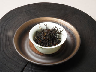 Yunnan Shaken-Leaf Black Tea dry leaves ready for Gong Fu brewing on a dark wooden board.