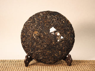 Front of unwrapped Jing Chang Hao Bada Ancient Trees 2013 raw Pu-erh 357g cake, dark arbor leaves with white inner label