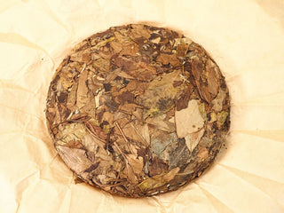 Unwrapped 2013 Fuding Sun-Dried Shou Mei 300g cake on wrapping paper, top view showing pressed mature leaves and stems.