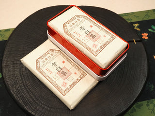 Open red tin box with a wrapped 2014 Fuding Shou Mei waffle cake inside, another wrapped cake displayed beside the box.