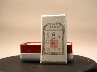 Open red tin box with a single 2014 Fuding White Peony waffle cake in paper wrapper, displayed beside the box.