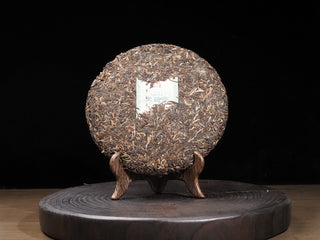Unwrapped 2016 Dayi 7532 raw Puerh tea cake front view on a wooden stand, showing tightly pressed young tea leaves and golden buds.